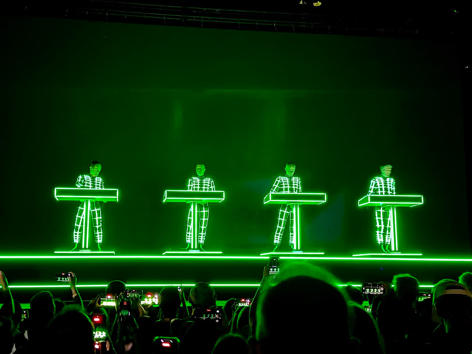Kraftwerk sahnede, neon ızgara kostümleriyle dört üye klavyelerinin başında